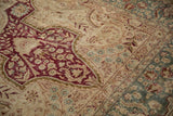 Detail of a distressed Kerman rug showing worn pile over burgundy red and dusty teal motifs.