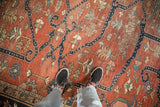 Antique Heriz carpet showing knot heads and sprawling navy vines on a brick-red field.