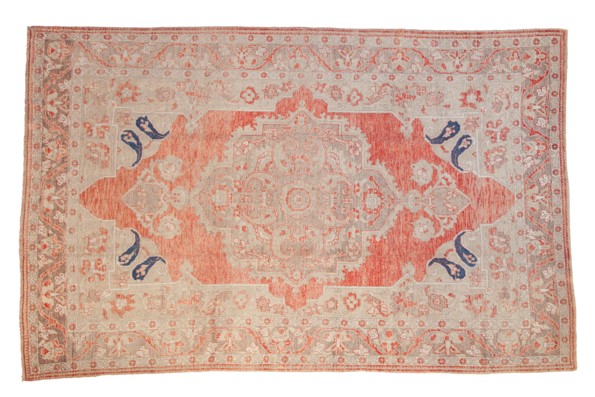 Distressed Turkish Oushak rug with a soft red medallion, silver-beige field, and bold navy botehs.