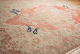Angled view of a distressed Oushak rug with navy blue boteh motifs on a soft red and beige field.