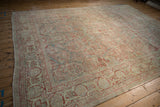Distressed antique Sarouk rug showing a border of faded red arabesque palmettes and even wear.