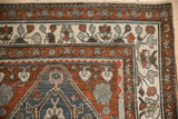 Corner detail of a distressed Persian rug with traditional borders in rust, charcoal, and ivory hues.