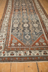 Angled view down the length of a distressed Hamadan runner with floral vine patterns.