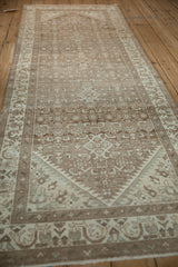 Angled view of a distressed Hamadan runner, highlighting its mostly even wear and pale coffee brown tones.