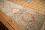 Perspective view of a distressed Heriz runner's stepped diamond medallions in red and powder blue.