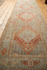 Long perspective view of a distressed Heriz runner with stepped diamond medallions in red and blue.