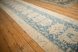 Angled view down the length of a distressed Persian runner with dusty teal and ivory geometric motifs.