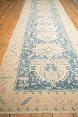 Angled view of a distressed Persian runner's length, showing teal geometric medallions on an ivory field.