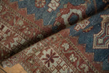Folded corner of a distressed Malayer runner showing the worn texture in indigo and pomegranate red.