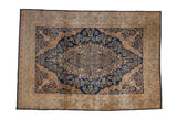 Vintage Kerman carpet with an ornate floral medallion on a navy blue field and wide, sand-colored borders.