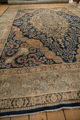 Low angle view of a vintage Kerman carpet's sand borders and navy blue floral field.
