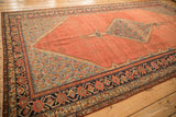 Angled view of a late 19th-century Malayer carpet detailing the blue corner spandrels and geometric vine border.