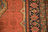 Close-up of the antique Malayer's red field, stepped contour, and geometric pomegranate vine border.