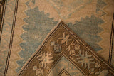 Folded corner of a distressed Caucasian runner showing the finned geometric border and hand-knotted weave.