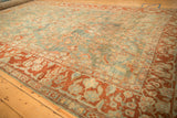 Angled view of an antique distressed Sarouk's terracotta border and dusty blue floral field.