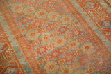 Angled view of a distressed Persian rug showing hexagonal guls in ochre, red, and powder blue.