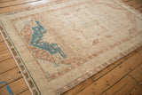 Angled view of a distressed Hamadan rug showing its concentric medallions in ivory, blue, and brown.