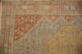 Corner view of a Persian rug's terra cotta spandrel and germinating plant motif border.