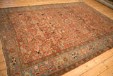 Full view of a vintage Persian Heriz carpet from an angle, showing its brick red field and wide sky blue border.