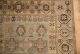 Corner of a distressed Hamadan runner with a geometric brown border and dusty blue field.