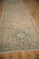 Angled view of a distressed Heriz runner with faded sand and seafoam geometric patterns.
