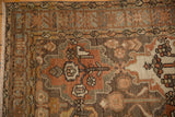 Corner detail of a distressed Bakhtiari rug with a geometric starburst border and low pile.