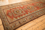 Angled view of a distressed Persian runner highlighting its geometric animal border and triple red medallions.