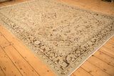 Angled view of a distressed Arak carpet showing worn floral blossoms in sand and brown tones.
