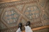 A person's view looking down at the distressed low pile and geometric pattern of a vintage Malayer runner.