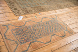 Distressed Belouch rug runner in terracotta and blue shown alongside another vintage rug on a wood floor.