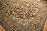 Angled view of a distressed Kaboutrahang carpet's corner, highlighting the floral pattern in brown and silver.