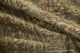 Textured, low-pile surface of a distressed Persian rug with dusty teal and camel Herati motifs.