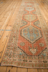 View down the length of a distressed Persian runner with repeating hexagonal medallions in soft reds and blues.