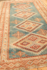 Angled view of a distressed Malayer rug's geometric diamond medallions on an abrashed blue field.