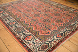 Angled view across a vintage Persian Malayer rug showing the brick red field and detailed pomegranate border.