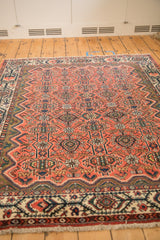 Angled perspective of a vintage Malayer rug showing its brick red field and geometric floral pattern.
