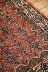 Detail of a vintage Malayer rug highlighting interconnected vines and serrated leaves on a brick red field.