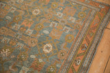 Detail of serrated leaf and vine motifs on a distressed rug's terracotta and blue borders.