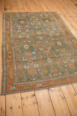 Angled view of a vintage distressed rug showing its geometric Herati design in earthy tones.