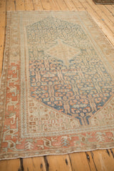 Vintage distressed Malayer rug from an angle, showing its blue quatrefoil pattern on a sand ground.
