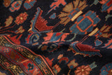 A fold in the vintage Persian rug shows the dense navy pile and large-scale palmettes.