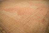 Distressed Oushak carpet's mostly even wear, featuring soft rose and pale gold tones.