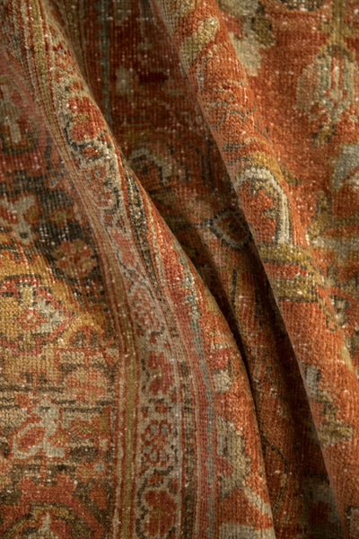 Soft folds of a distressed Mahal carpet showing its low, worn pile in madder root red and silver.