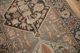 Distressed Bakhtiari rug texture with faded charcoal, tangerine, and cobalt floral-geometric patterns.