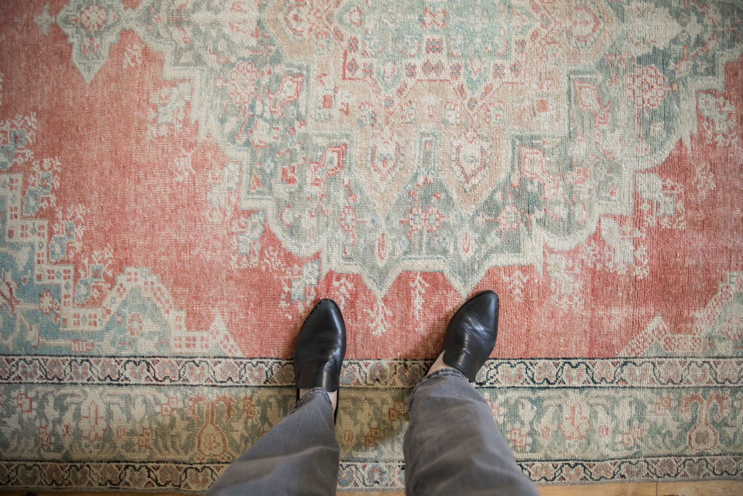 Detail of vintage distressed Anatolian rug, faded red and jade geometric patterns, visible foundation.