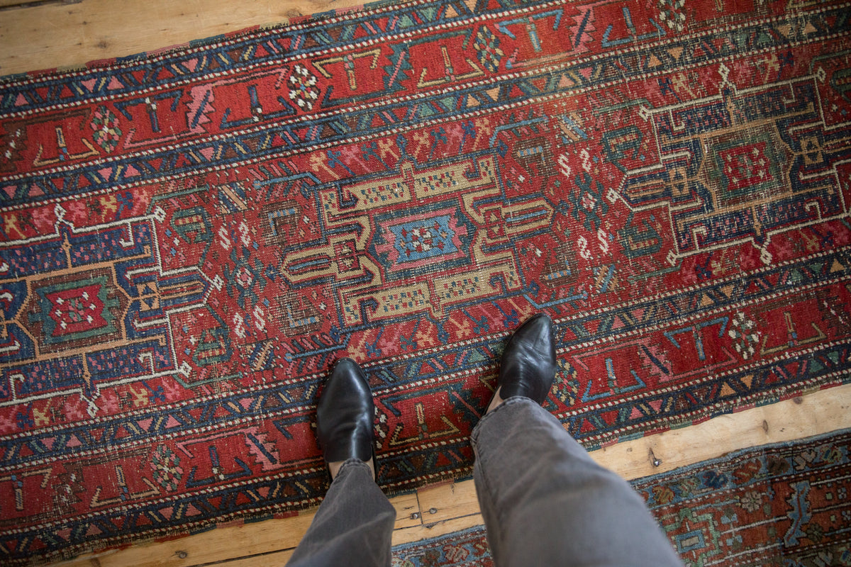 Feet on a Vintage Heriz runner, revealing Karaja geometric motifs in red, blue, and beige.