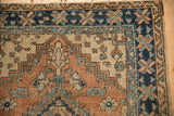 Corner of Heriz-area vintage rug: terracotta geometric leaves, navy pinwheel border, visible wear.