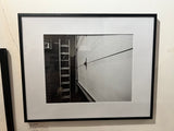 Different Perspective black and white photograph of a ladder and a textured door, shown in a black frame.