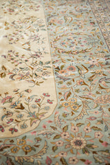 Ornate floral sprays and scrolling vinery on the vintage rug's ivory and pale blue fields.
