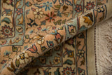 Rolled corner of a vintage Kerman rug showing its full pile, floral details, and ivory fringe.